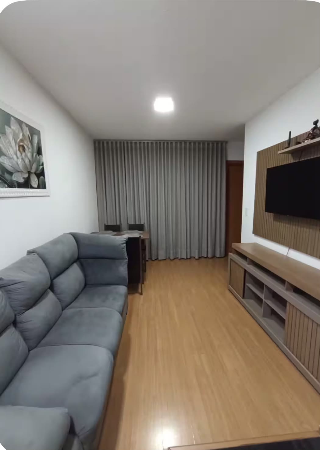 Sala com sofá cinza, painel de madeira e smart TV